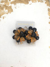 Load image into Gallery viewer, Clip on vintage earrings on original card with golden lettering spelling out ROCHELLE and CLIP. The earrings are layered plastic petal forms in black and orange plastic
