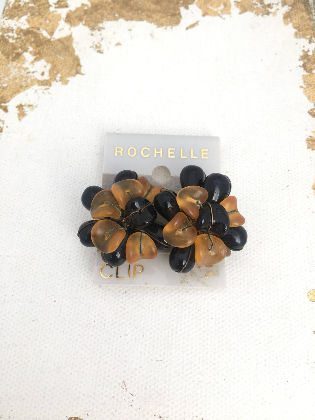 Clip on vintage earrings on original card with golden lettering spelling out ROCHELLE and CLIP. The earrings are layered plastic petal forms in black and orange plastic